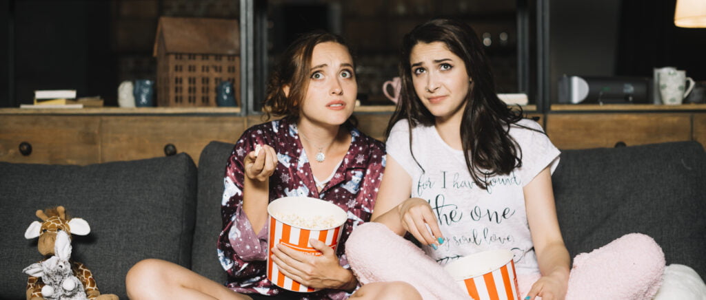 two-scared-women-sitting-sofa-with-popcorn-watching-television